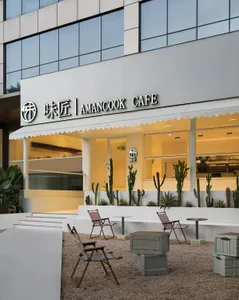 Modern cafe exterior with concrete walls, glass windows, and metal furniture.