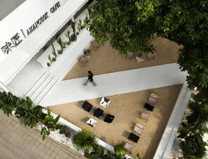 An aerial view of a minimalist cafe terrace featuring concrete tiles and palm trees, with tables and seating arranged around 