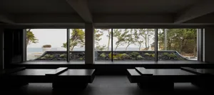 Interior of a modern hotel restaurant with dark wooden tables and view of the ocean through large windows.