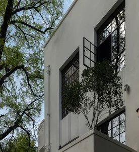 A modern residential building with a white concrete exterior, featuring large glass windows and greenery.