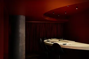A modern restaurant bar with dark interior design, wooden tables, and red accents.