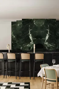 Modern interior of a restaurant bar featuring marble materials and high stools with woven seats.