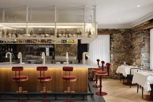 A modern restaurant bar featuring stone walls, wine shelves, red chairs, and sophisticated lighting.