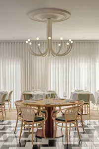 A modern dining room with wooden tables and chairs, white curtains, and a white chandelier.