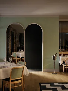 A modern restaurant interior with sleek, contemporary design elements, highlighted by a green wall with two arched doorways l