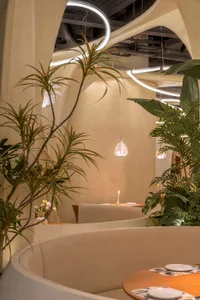 Modern restaurant interior with stylish design and green plants in the foreground.