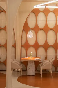 A modern restaurant interior featuring a table with a vase of flowers, surrounded by chairs on a terrazzo floor.
