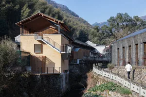 Modern architecture with wooden stairs and a stone wall in a natural setting.