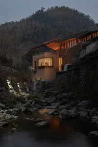 Modern residential house with wooden exterior, glass walls, and concrete foundation at night.