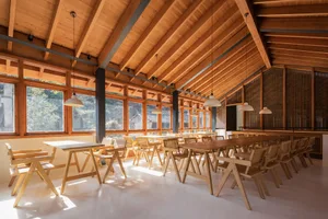 A spacious restaurant interior with wooden tables, chairs, and a high, wooden-beamed ceiling.