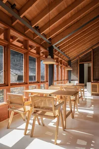 Modern restaurant interior with wooden tables and chairs, large windows, and natural light.