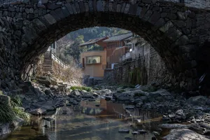 A stone bridge with an archway reflected in a calm waterway surrounded by natural elements.