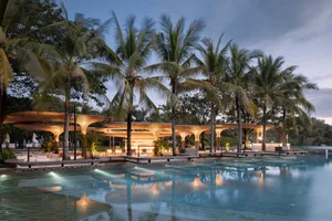 A beautiful tropical poolside bar illuminated with warm lighting, surrounded by palm trees at dusk.