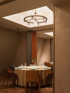 A restaurant interior with textured walls and leather seating, featuring a central circular light fixture with six pendant li