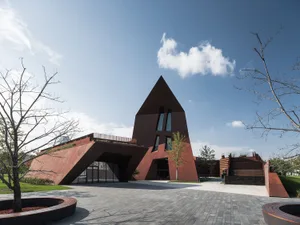 A modern, geometric building with a metallic exterior featuring large windows and a pointed roof.