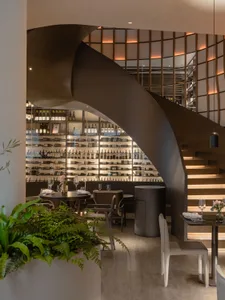 A modern restaurant bar featuring wooden materials and a spiral staircase with illuminated railings.