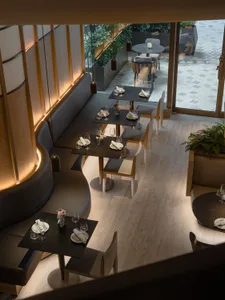 Modern restaurant interior with black tables, white chairs, and wooden flooring.