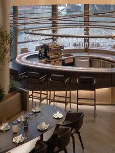 Modern industrial-style restaurant bar with wooden tables, metal stools, glassware, and glass counter.