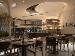 A modern restaurant interior featuring dark wood tables, leather chairs, glass shelves, and floral arrangements.