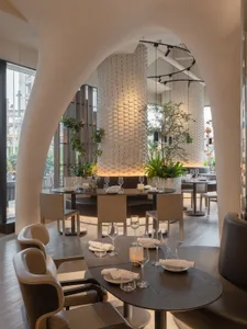 A modern restaurant interior featuring wooden tables, leather chairs, and indoor plants.