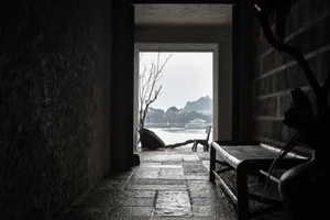 A dark, stone-walled interior with a wooden bench and view of a calm river and distant buildings.