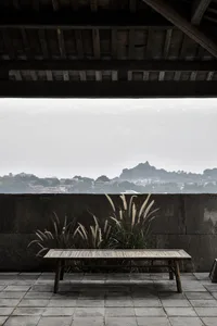 A wooden bench sits on a tiled rooftop with a view of a distant cityscape and a hill.