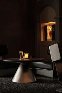 A casual bar area with a metal side table, black leather chairs, and a concrete floor.