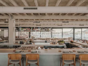 Industrial-style restaurant bar with concrete walls, open ceiling beams, and a range of drinks on the counter.