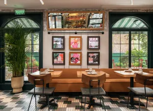 Industrial-style restaurant with a brown couch, potted plant, and framed art hanging on the wall.