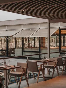 Modern industrial-style restaurant with wooden tables and chairs, glass walls overlooking a marina.