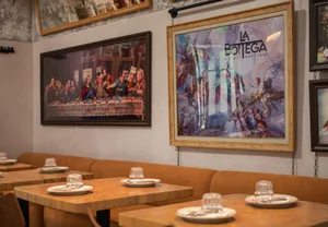 A restaurant interior with two paintings on the wall depicting a Last Supper scene and religious figures.