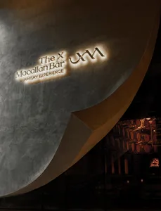 An illuminated macallan-bar-xjm-whisky-experience logo on a curved concrete exterior at night.
