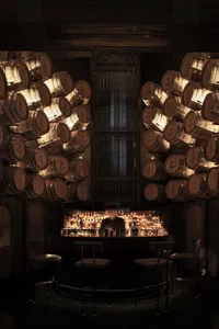 A modern bar interior with wooden barrels on the walls and a well-stocked bar counter.