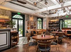 A modern cafe bar interior with wooden tables, metal chairs, and fabric seating.