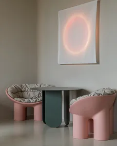 A modern lounge area featuring two pink, curved-plastic chairs with beige cushions and a small, round glass table in a minima
