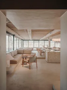 Modern restaurant interior with concrete flooring, large windows, and minimalist furniture.