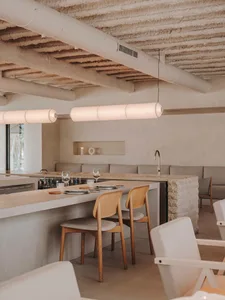 Modern restaurant interior with concrete counter bar, wooden chairs, and white pendant lights.