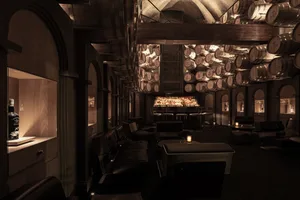 An industrial-style bar lounge with metal barrels hanging from the ceiling and a bar counter in the background.