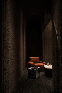 A modern hallway with textured concrete walls and a single orange armchair with a cowhide ottoman and small table.