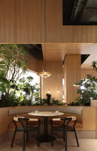 A cozy cafe interior featuring wooden walls and ceiling, plant decoration, and a round table with chairs.