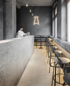 A modern restaurant interior featuring a concrete bar counter with metal stools and a minimalist design aesthetic.