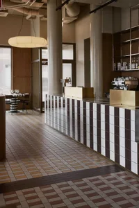 A minimalist coffee shop interior with a tiled counter and a modern hanging light fixture.