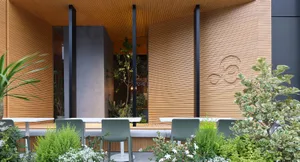 Outdoor seating area with green chairs and white tables at a restaurant with a modern design in wood.