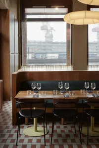 A modern restaurant interior with wooden tables, leather chairs, and large windows overlooking a harbor.