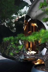 A modern restaurant interior with a circular mirrored metal sculpture and bonsai tree, offering a sophisticated dining experi