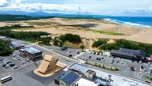 Aerial view of a coastal town center featuring a sand dune landscape, beach, and buildings with adjacent parking areas.