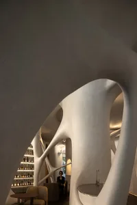 A modern restaurant bar featuring light concrete architecture with curved and organic shapes.