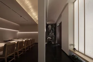 Contemporary minimalist restaurant interior with wood tables, marble accents, and dark slate flooring.
