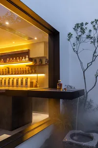 A sleek, modern bar counter with a concrete base and metal structure, featuring illuminated shelves and a water feature in th