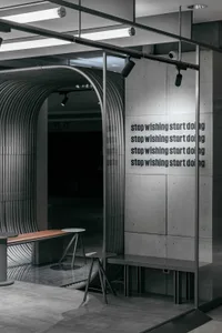 The minimalist café features concrete walls and a modern seating area with a glass enclosure.